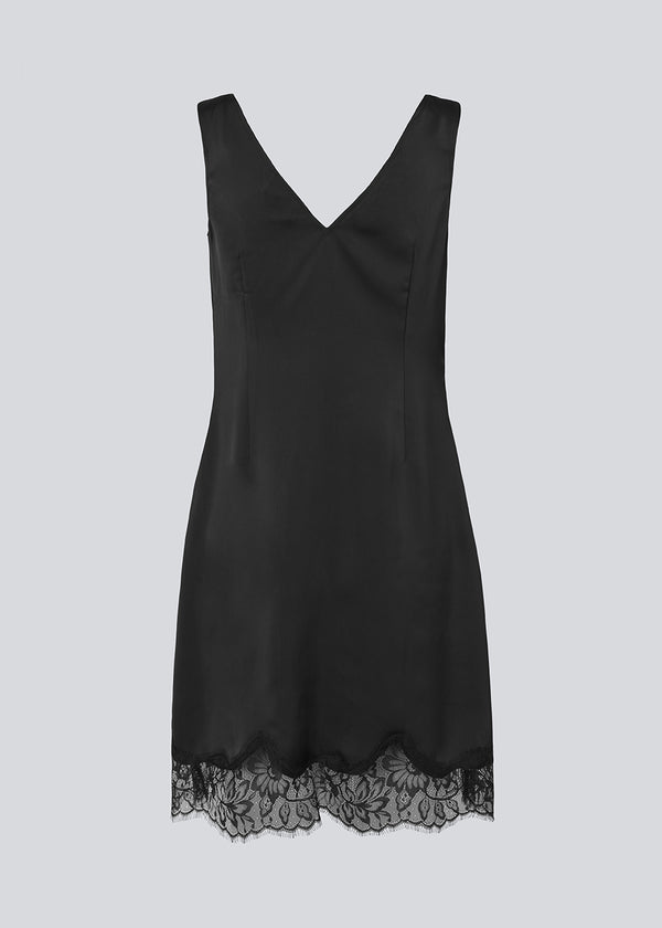 Kort sort satinkjole med blonde detaljer i bunden og over brystet. Vuemd Dress har brede stropper, krydsdetalje med blonder over brystet og en skjult lynlås i siden. En elegant og feminin style, der er perfekt til både hverdag og fest.