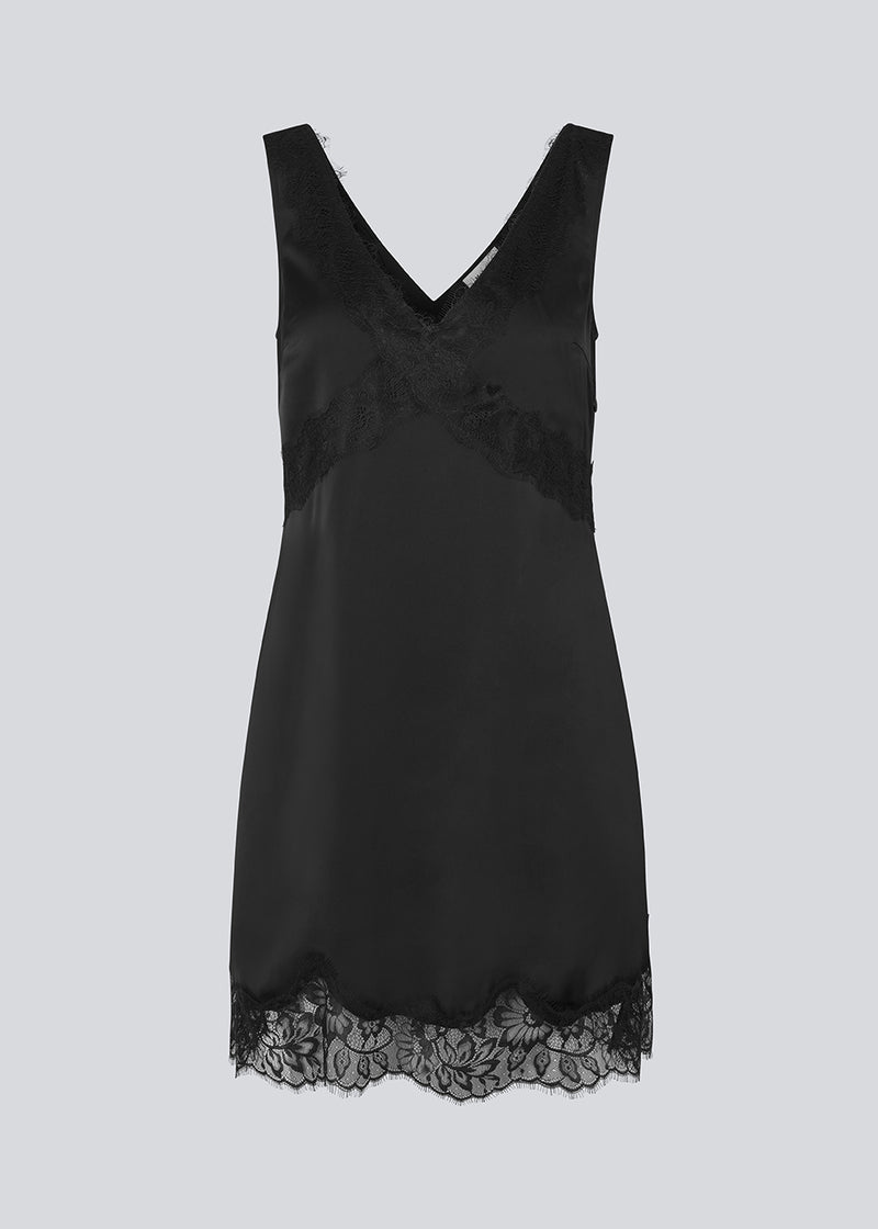 Kort sort satinkjole med blonde detaljer i bunden og over brystet. Vuemd Dress har brede stropper, krydsdetalje med blonder over brystet og en skjult lynlås i siden. En elegant og feminin style, der er perfekt til både hverdag og fest.