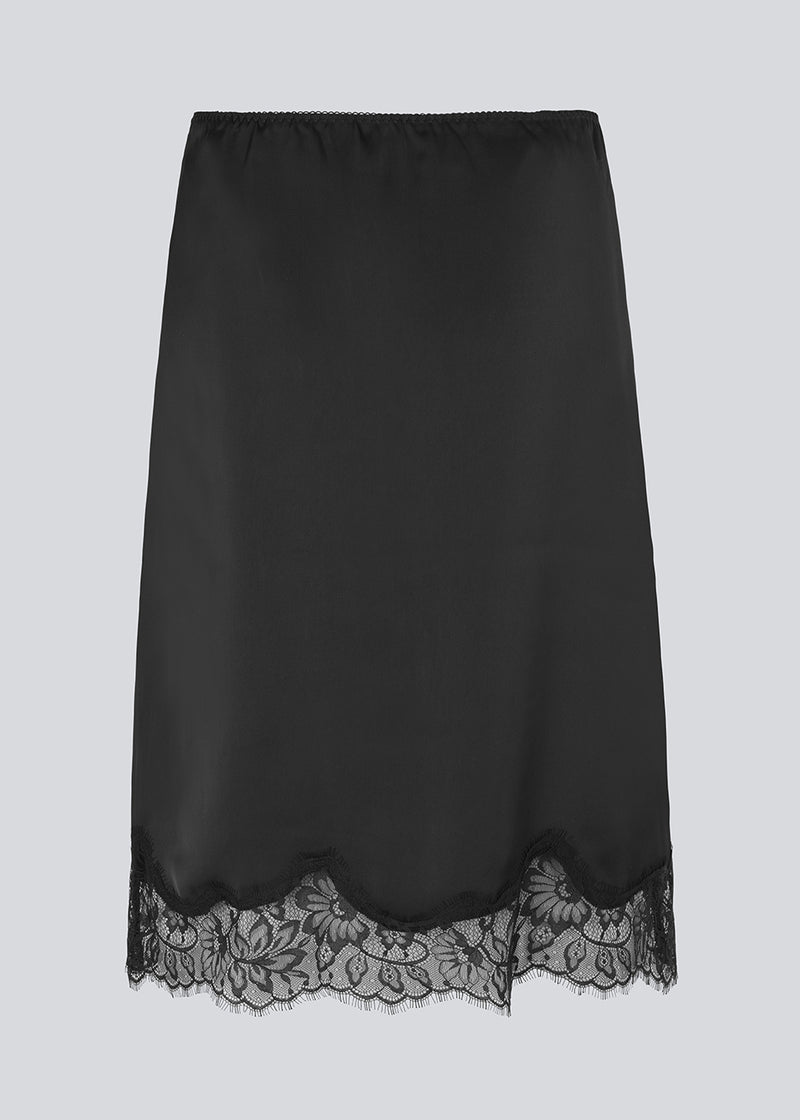 Sort satin nederdel med blondedetaljer i bunden. Vuemd skirt er knælang med eleastik i taljen og har en afslappet pasform. Ideel alene eller stylet som en del af en lag-på-lag styling.