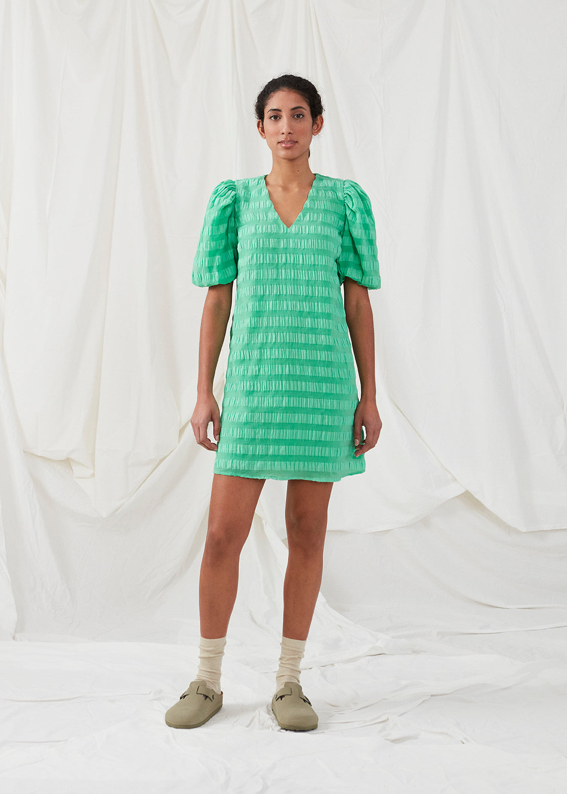Kort kjole i grøn designet i et bæk og bølge materiale. DinoMD dress har v-udskæring i halsen, en løs pasform og korte puffærmer med elastik. Modellen er 177 cm og har en størrelse S/36 på.