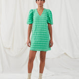 Kort kjole i grøn designet i et bæk og bølge materiale. DinoMD dress har v-udskæring i halsen, en løs pasform og korte puffærmer med elastik. Modellen er 177 cm og har en størrelse S/36 på.