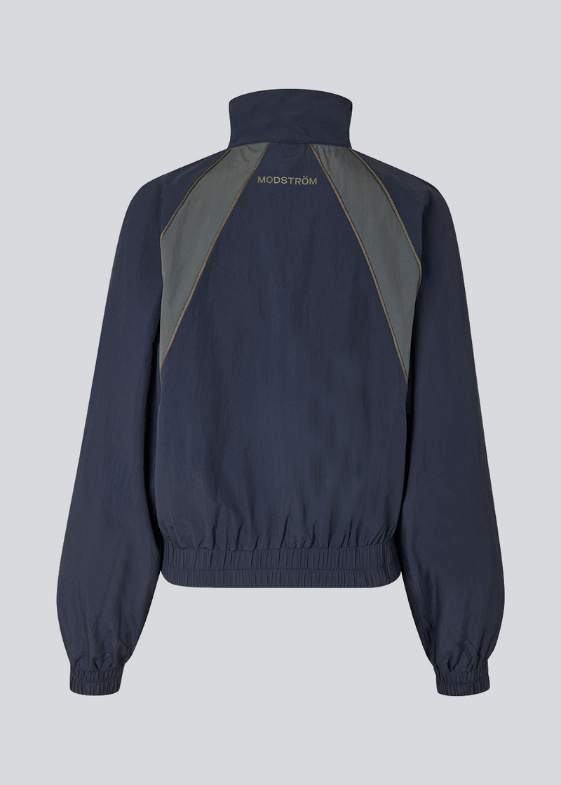 Mørkeblåt tracksuit jakke i 100% genanvendt nylon. Volmermd jacket har kontrastpaneler, høj hals og lynlåslukning fortil.&nbsp;&nbsp;