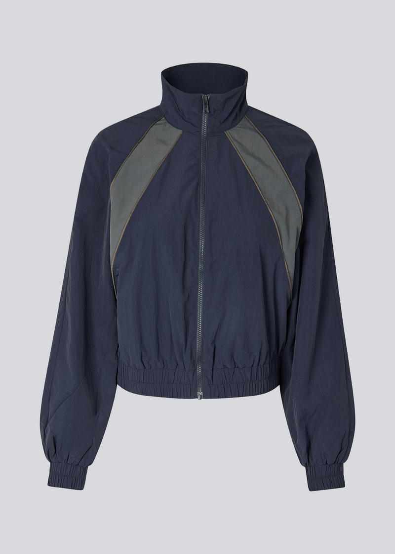 Mørkeblåt tracksuit jakke i 100% genanvendt nylon. Volmermd jacket har kontrastpaneler, høj hals og lynlåslukning fortil.&nbsp;&nbsp;