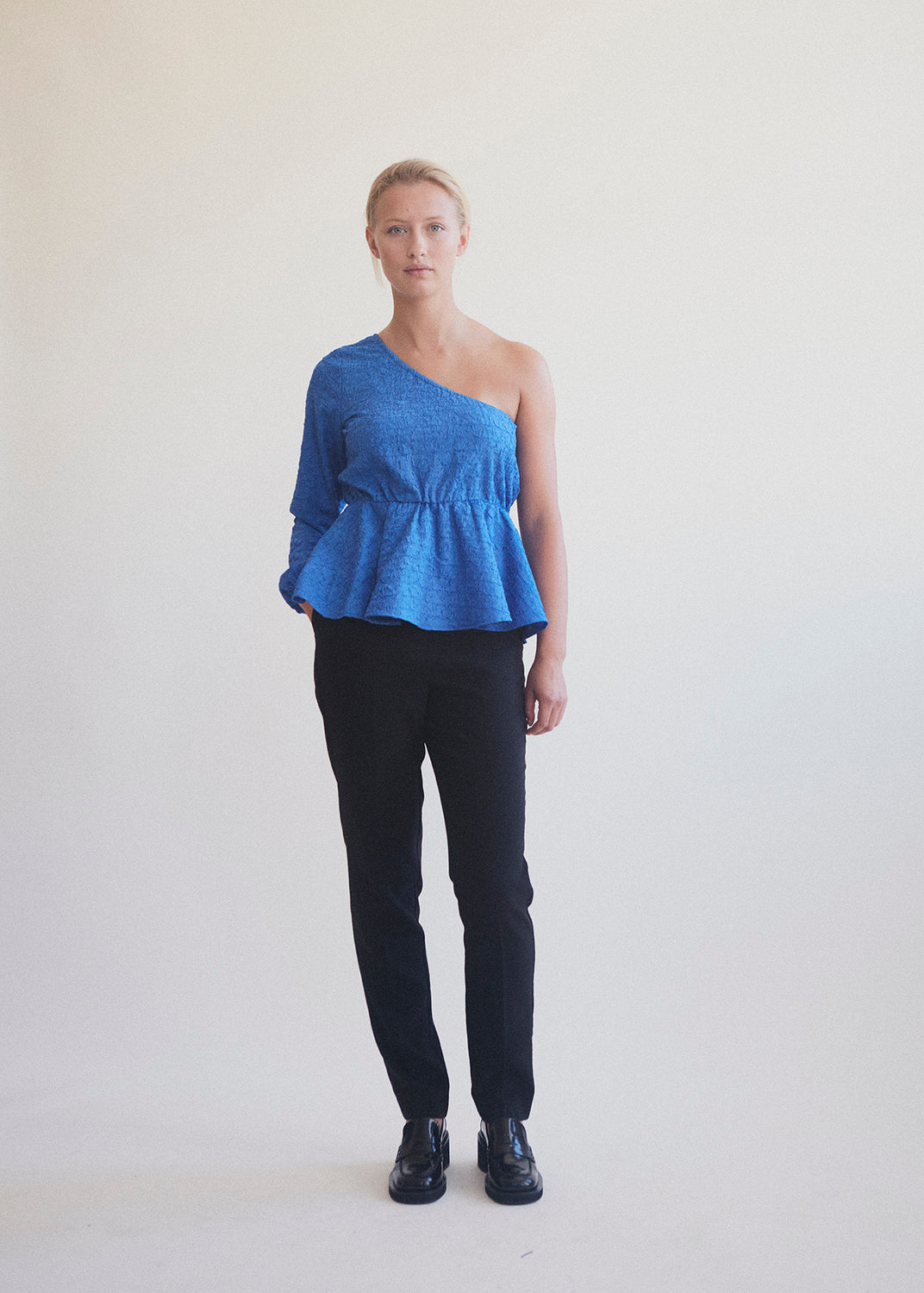 One shoulder top med et langt ærmer med puf og elastisk manchet. TalissaMD top er designet i et struktureret materiale med elastisk peplum-effekt ved taljen.