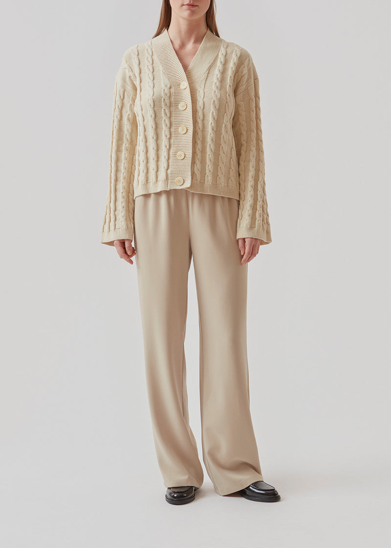 Cardigan i beige i kabelstrik med lange ærmer. AliceMD cardigan har v-udskæring og knapper foran. Ribkanter langs udskæring, knapper, manchet og bund.