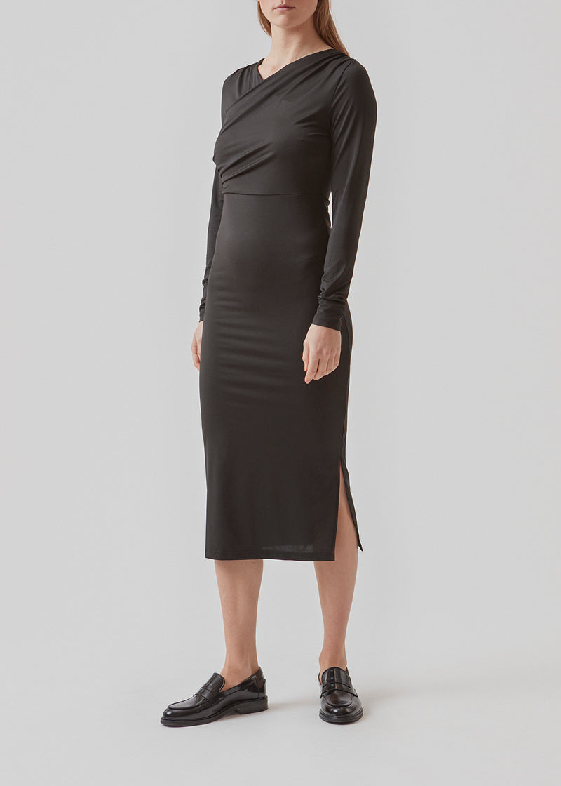 Tætsiddende kjole i sort med langt skørt med slidser i siderne. ArniMD dress har en høj v-udskæring med flatterende wrap-detalje over brystet.