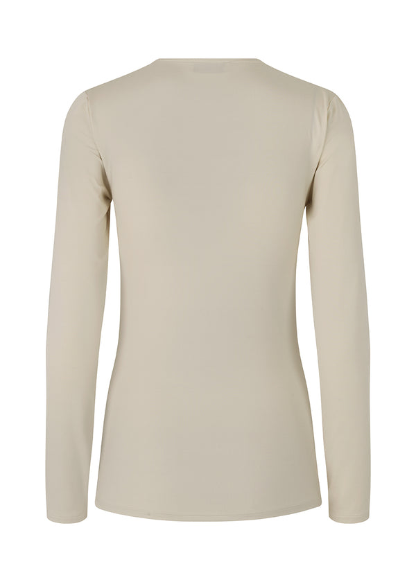 Langærmet bluse i beige med kropsnær pasform og i elastisk materiale. ArniMD top har en høj v-udskæring med wrap-effekt foran.
