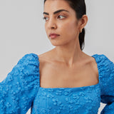 Kort kjole i blå med all-over blomstermotiv. AtiraMD dress har lange ballonærmer med en mere kropsnær krop. Halsudskæringen er firkantet både foran og bagpå.  Modellen er 177 cm og har en størrelse S/36 på.