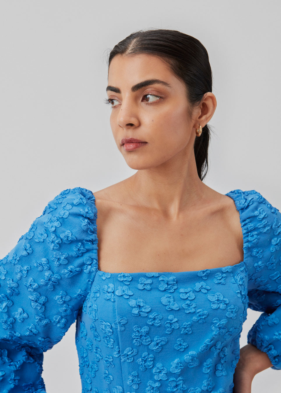 Kort kjole i blå med all-over blomstermotiv. AtiraMD dress har lange ballonærmer med en mere kropsnær krop. Halsudskæringen er firkantet både foran og bagpå.  Modellen er 177 cm og har en størrelse S/36 på.