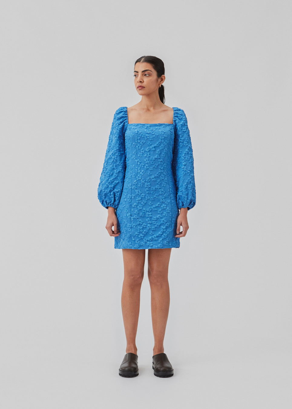 Kort kjole i blå med all-over blomstermotiv. AtiraMD dress har lange ballonærmer med en mere kropsnær krop. Halsudskæringen er firkantet både foran og bagpå.  Modellen er 177 cm og har en størrelse S/36 på.