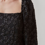 Kort kjole i sort med all-over blomstermotiv. AtiraMD dress har lange ballonærmer med en mere kropsnær krop. Halsudskæringen er firkantet både foran og bagpå.