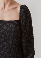 Kort kjole i sort med all-over blomstermotiv. AtiraMD dress har lange ballonærmer med en mere kropsnær krop. Halsudskæringen er firkantet både foran og bagpå.