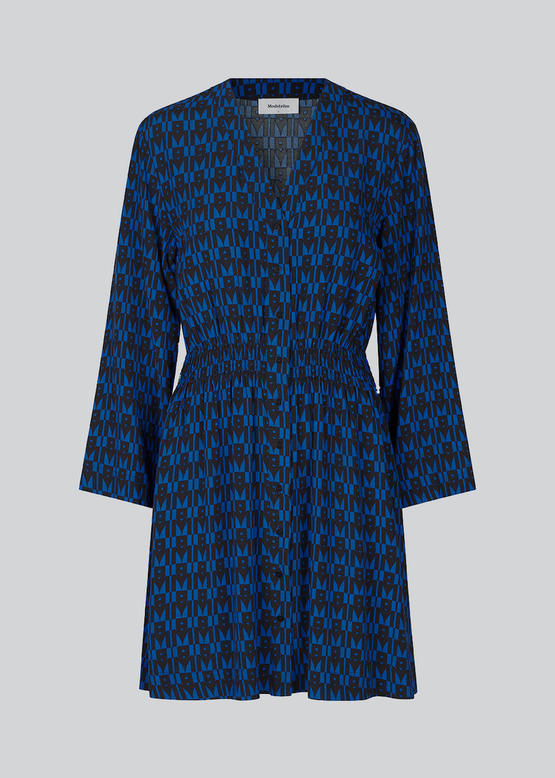 Kort kjole i farven: Graphic Heart Bright Ocean, i mere ansvarlig kvalitet med print. BorysMD print dress har dyb v-udskæring med knaplukning fortil og smock-detalje ved taljen. Lange, brede ærmer.