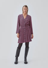 Kort kjole i farven: Graphic Heart Cosmos Pink, i mere ansvarlig kvalitet med print. BorysMD print dress har dyb v-udskæring med knaplukning fortil og smock-detalje ved taljen. Lange, brede ærmer.