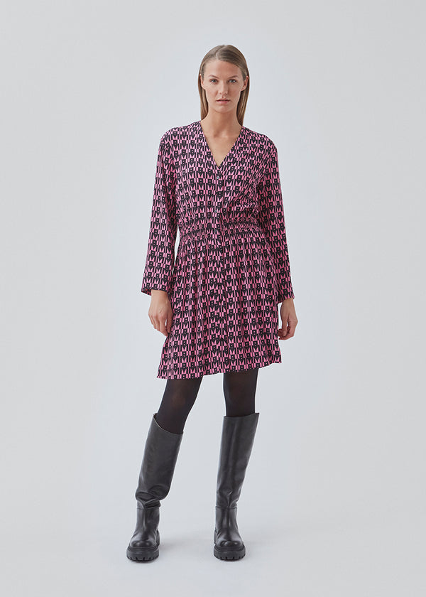 Kort kjole i farven: Graphic Heart Cosmos Pink, i mere ansvarlig kvalitet med print. BorysMD print dress har dyb v-udskæring med knaplukning fortil og smock-detalje ved taljen. Lange, brede ærmer.
