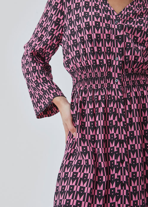 Kort kjole i farven: Graphic Heart Cosmos Pink, i mere ansvarlig kvalitet med print. BorysMD print dress har dyb v-udskæring med knaplukning fortil og smock-detalje ved taljen. Lange, brede ærmer.