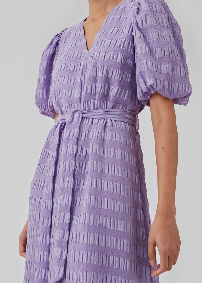 Lang kjole i struktureret stof. CalieMD dress har korte pufærmer, v-halsudskæring og bindebælte i taljen.  Modellen er 177 cm og har en størrelse S/36 på.