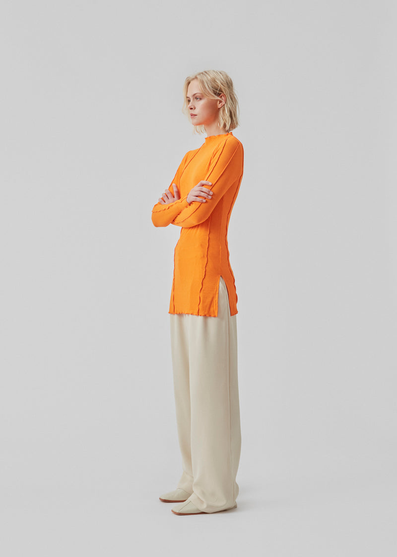 Bluse i orange med høj hals og synlige sømdetaljer i let og blødt materiale. CassieMD LS top er en tætsiddende top med lange ærmer og slidser i siderne. Modellen er 177 cm og har en størrelse S/36 på.