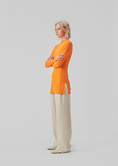 Bluse i orange med høj hals og synlige sømdetaljer i let og blødt materiale. CassieMD LS top er en tætsiddende top med lange ærmer og slidser i siderne. Modellen er 177 cm og har en størrelse S/36 på.