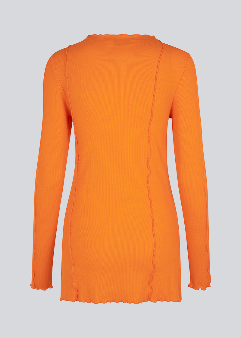 Bluse i orange med høj hals og synlige sømdetaljer i let og blødt materiale. CassieMD LS top er en tætsiddende top med lange ærmer og slidser i siderne. Modellen er 177 cm og har en størrelse S/36 på.
