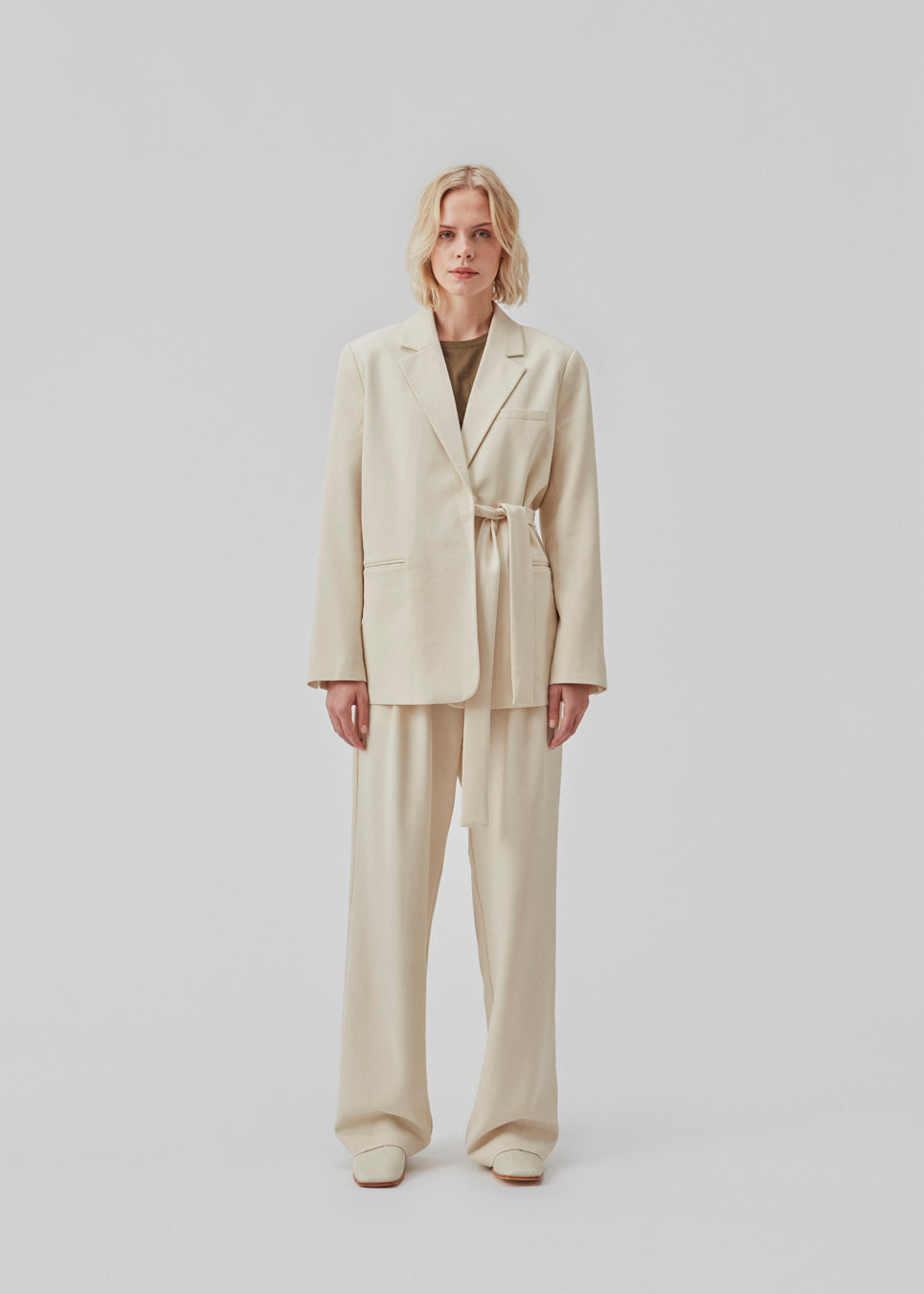 Løse bukser i beige med brede ben, der er fremstillet af genanvendte materialer. Dobbelte plisseringer foran, lynlåsgylp og knaplukning. Modellen er 177 cm og har en størrelse S/36 på.  Style med den matchende blazer: CayaMD blazer.