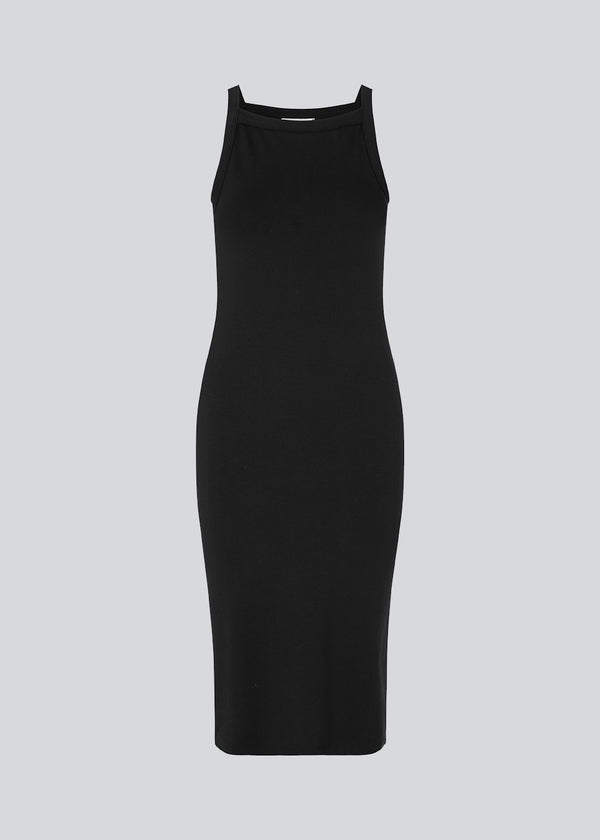 Tætsiddende basic sort kjole i en økologisk bomuldsjersey. DaeMD dress er uden ærmer og har en høj og lige halsudskæring. Kjolen skærer under knæene. Modellen er 177 cm og har en størrelse S/36 på.