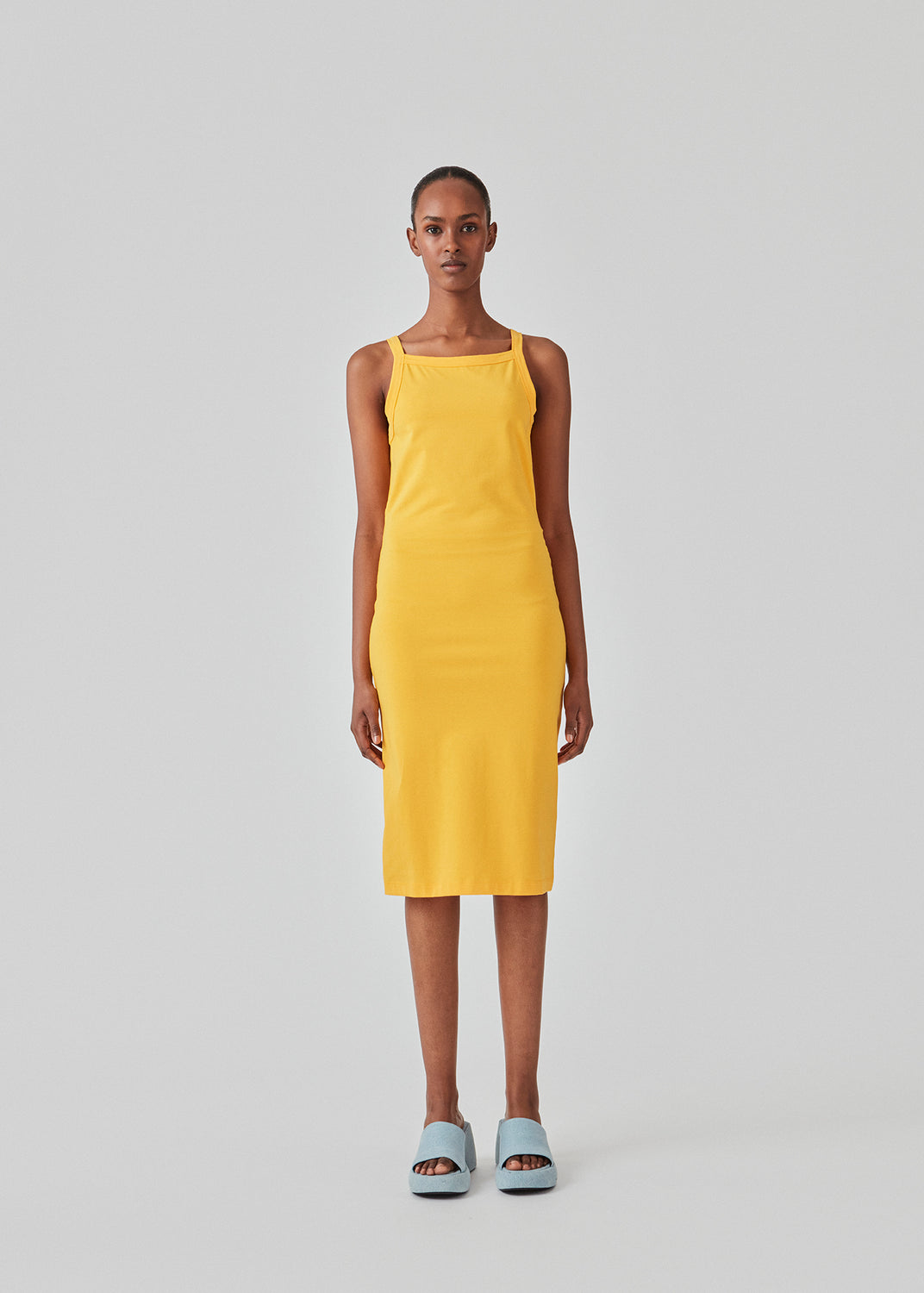 Tætsiddende basic gul kjole i en økologisk bomuldsjersey. DaeMD dress er uden ærmer og har en høj og lige halsudskæring. Kjolen skærer under knæene. Modellen er 177 cm og har en størrelse S/36 på.