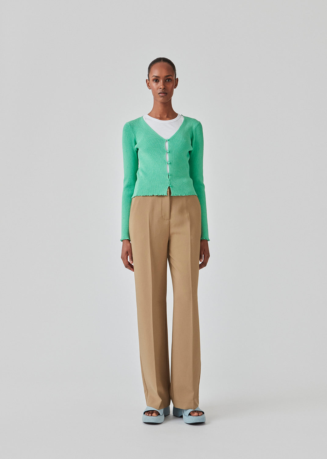 Tætsiddende, let cropped cardigan i grøn med knaplukning foran. DorisMD cardigan har en dybrund halsudskæring, lange ærmer og bølgekanter i bund og ved manchet. Modellen er 177 cm og har en størrelse S/36 på.