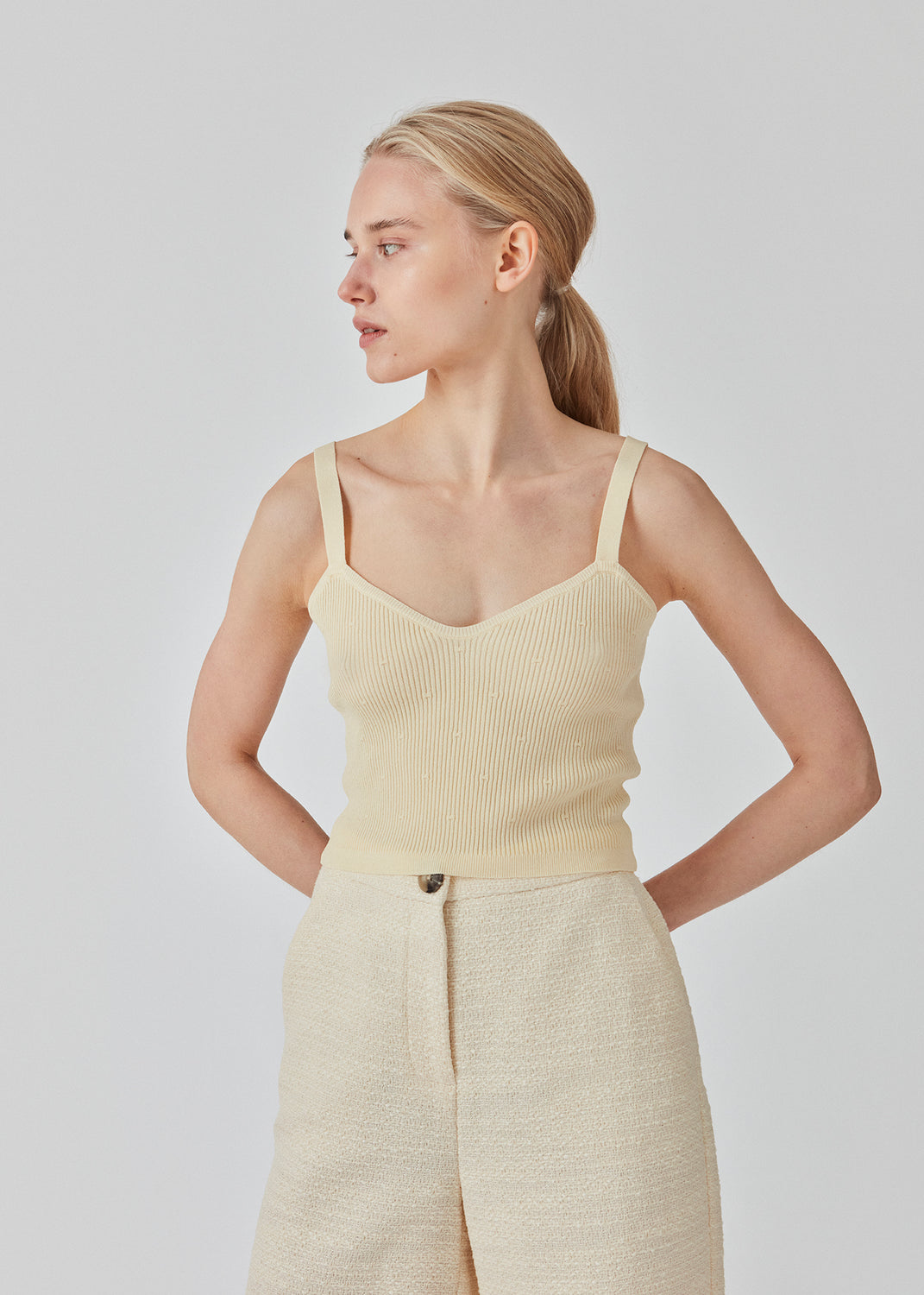 Råhvid crop top i ribstrikket kvalitet. DorisMD top har smalle stropper, v-udskæring oget tætsiddende fit. Modellen er 177 cm og har en størrelse S/36 på.