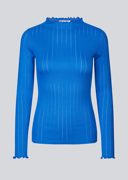 Tætsiddende trøje i blå med mellem høj krave. Issy t-neck har feminine flæsekanter ved hals og ærmer. Kvaliteten er en blød jersey med et feminint pointelle mønster.