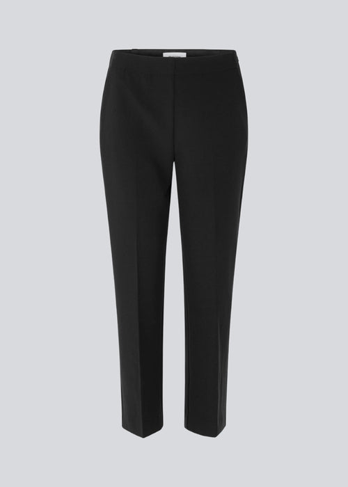 Klassiske bukser i sort med pressefolder og lige afkortede ben. NelliMD cropped pants lukkes med en skjult lynlås i siden og har en skjult elastik i taljen for et mere komfortabelt fit. Modellen er 173 cm og har en størrelse S/36 på