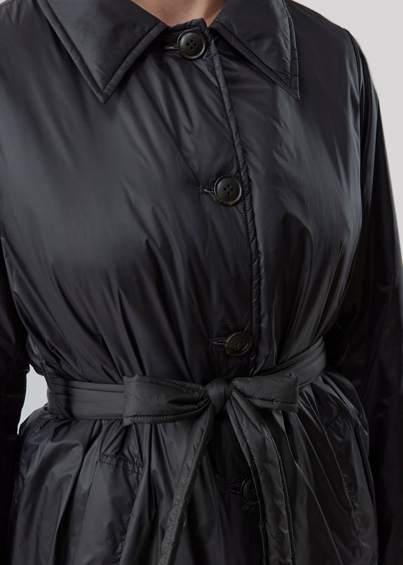 Sporty frakke med krave, knapper og taljebælte. Oma jacket er en cool nylonfrakke i en rummelig men feminin pasform. Frakkens lette fyld er 100% genanvendt polyester. Modellen er 173 cm og har en størrelse S/36 på