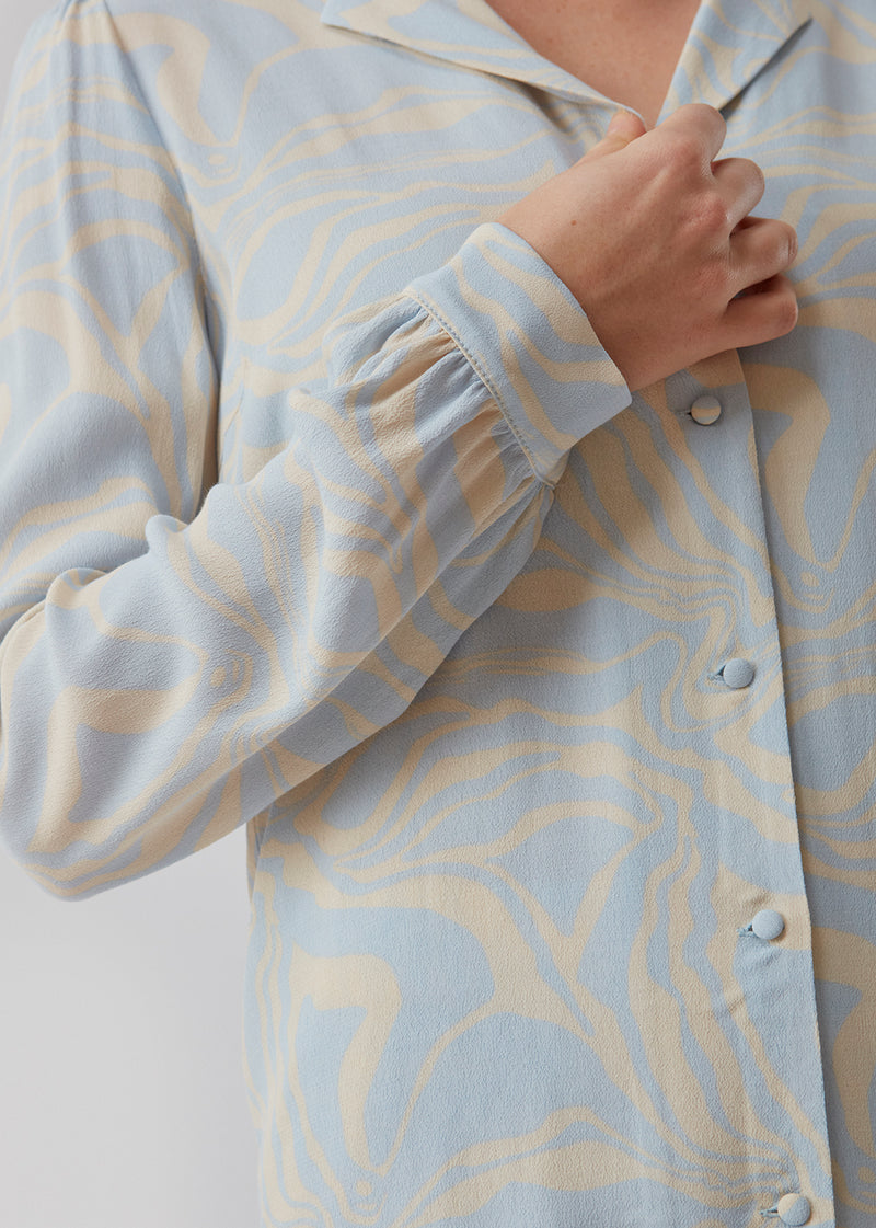 Palm print shirt har et organisk print i en kvalitet af EcoVero viskose. Skjorten har en løs pasform med lange ærmer, v-udskæring og stofbetrukne knapper. Modellen er 173 cm og har en størrelse S/36 på