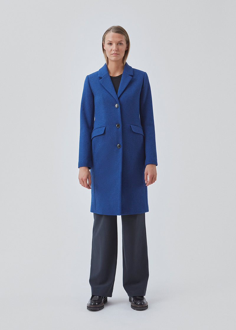 Smuk knælang uldfrakke i flot blå. Pamela coat bliver knappet fortil af 3 store knapper og er taljeret, som giver et feminint udtryk. På grund af den høje kvalitet af uld, vil den være det oplagte valg at bruge til både efterår og de milde vintre.