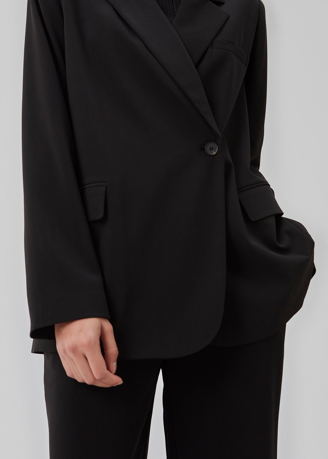 Sort blazer i et oversize fit med et asymmetrisk look. PerryMD blazer er i en let kvalitet, som kan styles med de matchende bukser eller over en kjole på en sommeraften. Indersøm (S/36): 81 cm Bukserne forlænges med 0,5 cm for hver størrelse. Modellen er 173 cm og har en størrelse S/36 på.  Shop matchende bukser, for at fuldende looket: PerryMD pants.