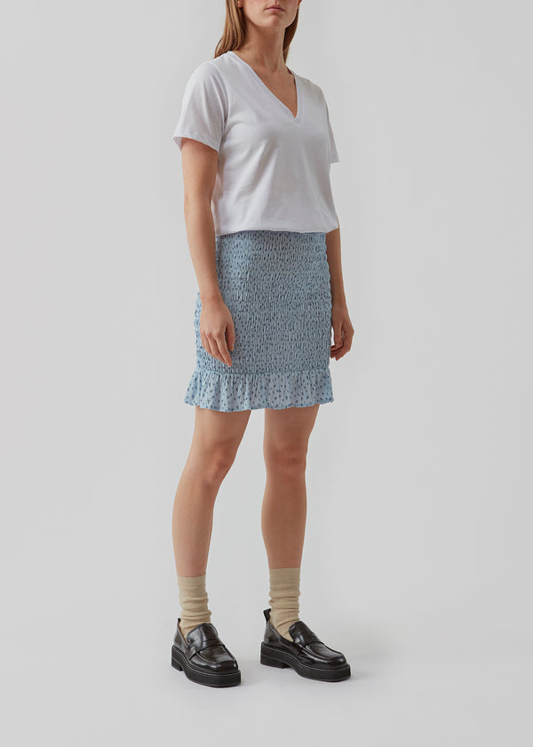 Porscha print skirt er en kort nederdel med elastisk smock over hele skørtet, som afsluttes med en bred flæsekant. Det blomsterprintede materiale er en EcoVero viskosekvalitet. Modellen er 173 cm og har en størrelse S/36 på