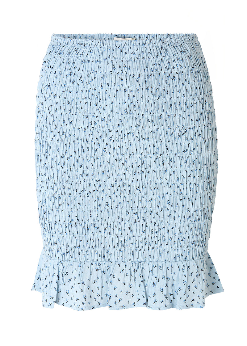 Porscha print skirt er en kort nederdel med elastisk smock over hele skørtet, som afsluttes med en bred flæsekant. Det blomsterprintede materiale er en EcoVero viskosekvalitet.