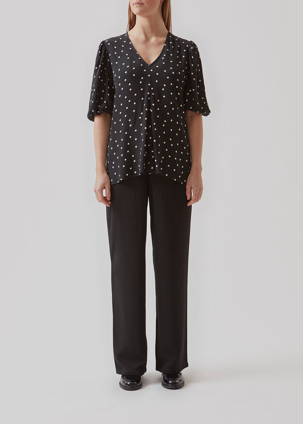 Bluse i en mere ansvarlig kvalitet i sort med prikker. RidderMD print top har korte pufærmer og v-udskæring. Den voluminøse pasform detaljeres med et wienerlæg foran. Modellen er 173 cm og har en størrelse S/36 på.