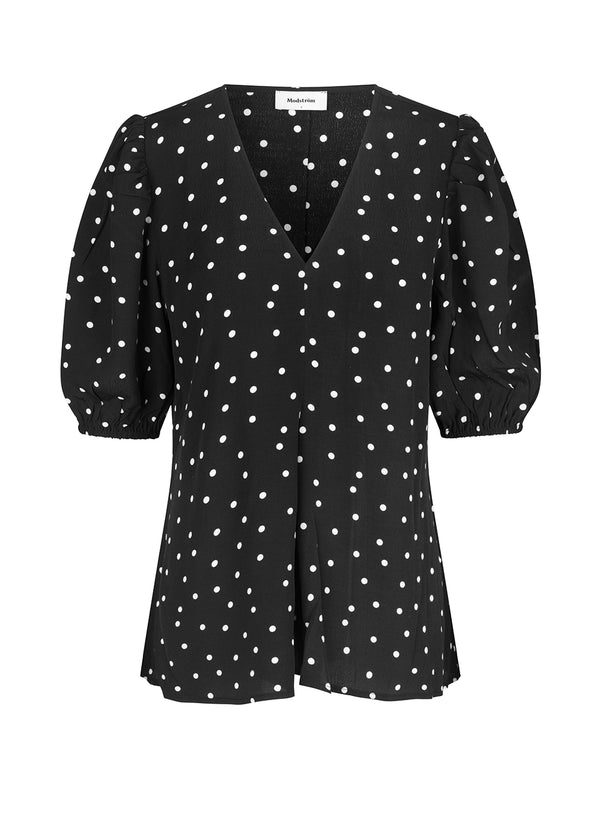 Bluse i en mere ansvarlig kvalitet i sort med prikker. RidderMD print top har korte pufærmer og v-udskæring. Den voluminøse pasform detaljeres med et wienerlæg foran. Modellen er 173 cm og har en størrelse S/36 på.