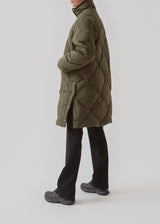 Quiltet jakke med fyld af duni grøn. ScarlettMD jacket er en knælang jakke med høj opretstående krave, samt lynlås og vindslå med trykknapper. Jakken har to forlommer med flap og trykknap og elastik nederst på ærmerne. Modellen er 177 cm og har en størrelse S/36 på.