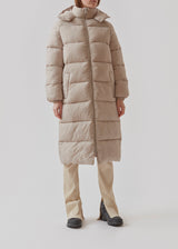 Knælang frakke i beige i vatteret nylon. StellaMD long jacket har en afslappet pasform med lange ærmer, hætte og opretstående krave. Tovejslynlås, justerbar hætte og diskrete sidelommer.