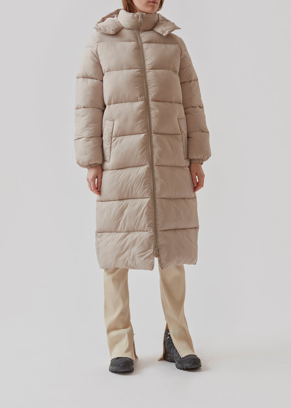 Knælang frakke i beige i vatteret nylon. StellaMD long jacket har en afslappet pasform med lange ærmer, hætte og opretstående krave. Tovejslynlås, justerbar hætte og diskrete sidelommer.