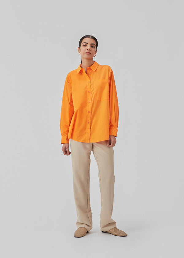 Luftig orange skjorte i økologisk bomuldspoplin i orange. TapirMD shirt har krave og knapper foran, samt åben brystlomme. Lav skuldersøm og lange ærmer med manchet og knap. Broderet logo foran.  Modellen er 177 cm og har en størrelse S/36 på.