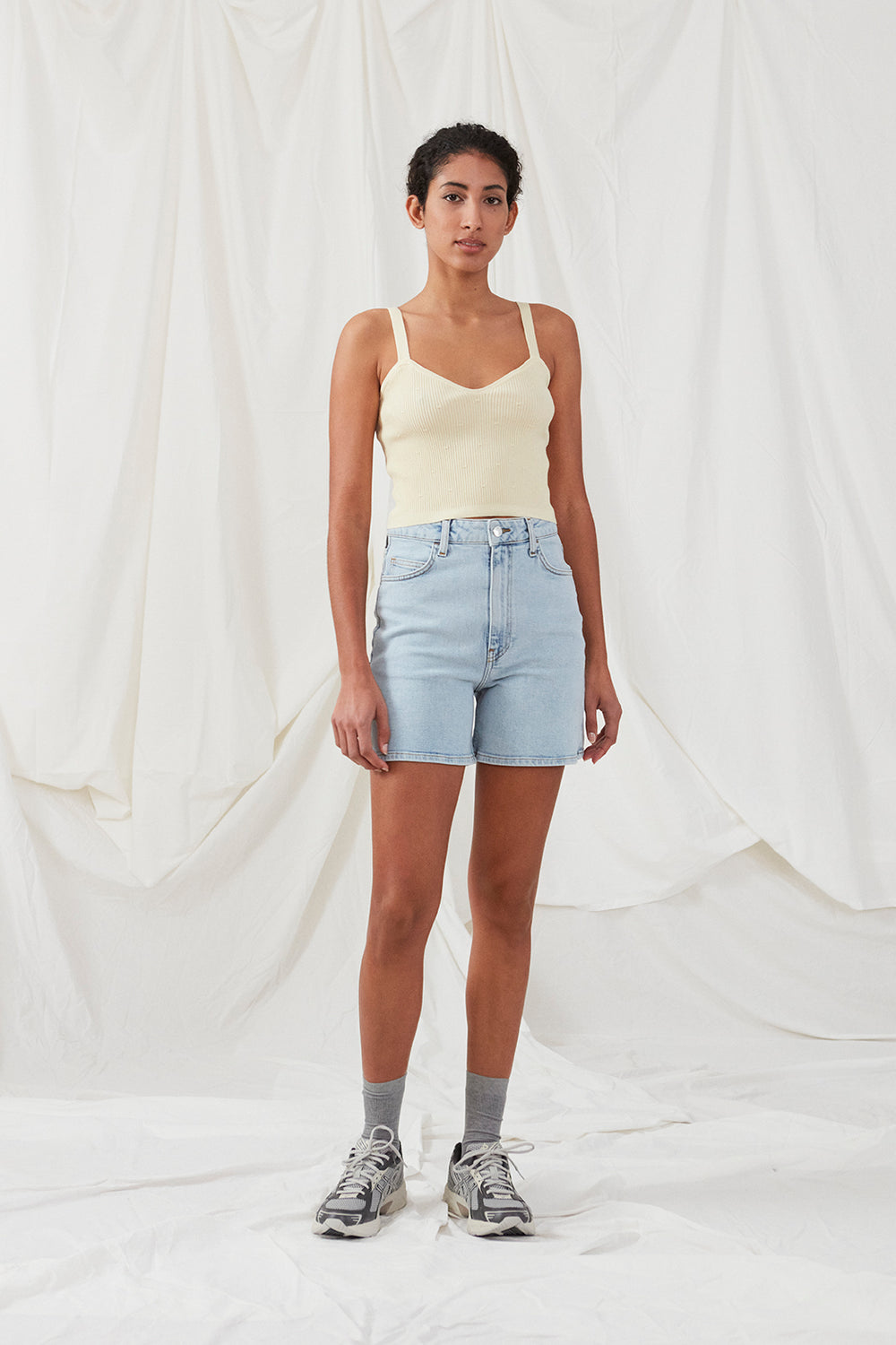 Råhvid crop top i ribstrikket kvalitet. DorisMD top har smalle stropper, v-udskæring oget tætsiddende fit. Modellen er 177 cm og har en størrelse S/36 på.